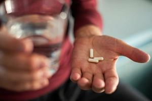 persona con vaso de alcohol y cápsulas de suplementos